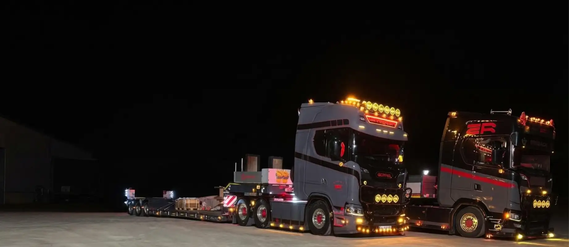 Zwei Scania-Zugmaschinen mit Tieflader bei Nacht, mit dem roten ER